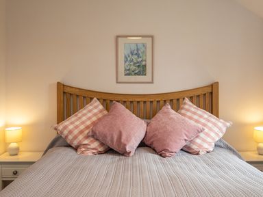 A bed with a wooden headboard and four pink cushions two bedside tables with lamps and a framed floral painting on the wall at Hazelhurst in Rock