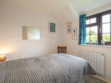 A bedroom with a bed covered in a gray quilt next to a window with blue curtains and three small plants on the windowsill at Hazelhurst in Rock