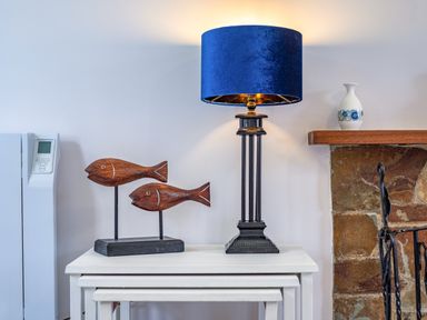 A side table with wooden fish sculptures and a lamp with a blue shade next to a stone fireplace at Hazelhurst in Rock