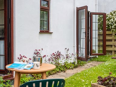 A garden with green grass daisies and small flowers along a white wall with wooden framed windows and a wooden table with mugs and a teapot at Hazelhurst in Rock