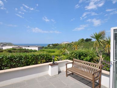 An outdoor space with a bench and plants overlooking the sea at Sunset in Polzeath