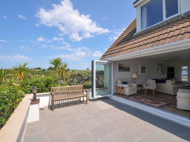An outdoor terrace with bench and sliding door at Sunset in Polzeath