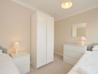 A bedroom with a wardrobe, lamp, mirror, and chest of drawers at Sunset in Polzeath