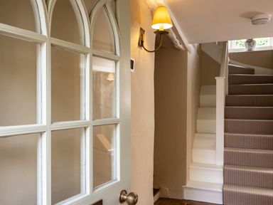 A staircase with a striped carpet and a wall lamp next to a door with glass panels at Porthilly Greys in Rock