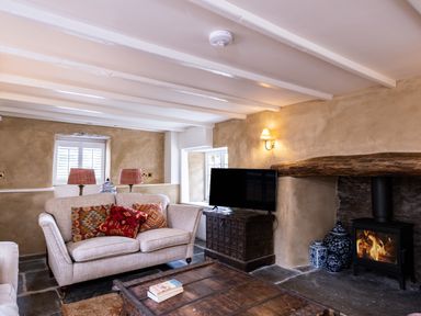 A sitting room with a beige sofa with patterned cushions a wooden coffee table a television on a wooden cabinet and a wood burning stove at Porthilly Greys in Rock