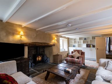 A living room with a wood-burning stove a wooden coffee table armchairs and built-in shelves at Porthilly Greys Rock