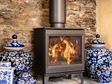 A wood burning stove with fire inside flanked by blue and white decorative ceramic jars at Porthilly Greys in Rock