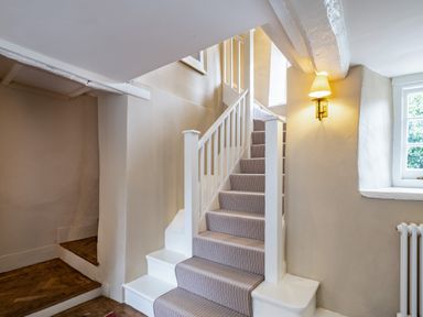 A staircase with a striped carpet runner and white wooden railing beside a wall with a light fixture and a window at Porthilly Greys in Rock