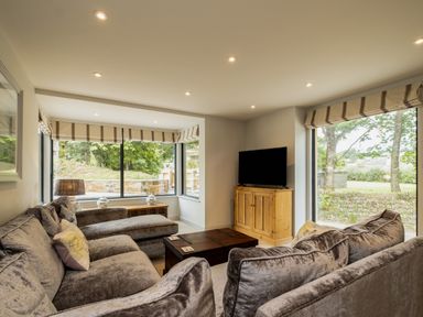 A living room with large windows two sofas a wooden TV cabinet and a wooden coffee table at Porthilly Greys in Rock