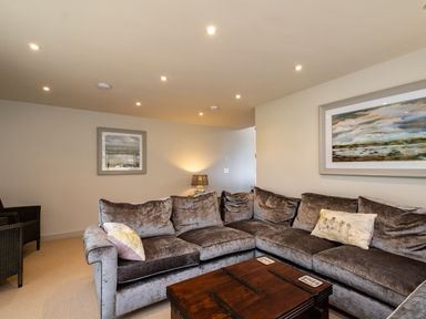 A living room with a large sectional sofa a wooden chest coffee table framed paintings on the walls and a lamp on a side table at Porthilly Greys in Rock