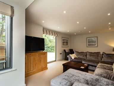 A living room with a large sofa a wooden TV cabinet a television a wooden coffee table and framed pictures on the wall at Porthilly Greys Rock