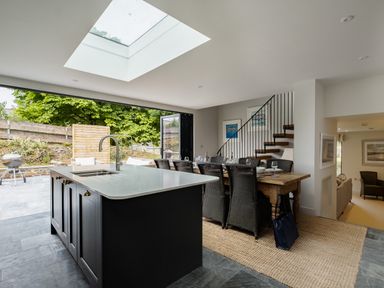 A kitchen island with sink and faucet next to a dining table with chairs and staircase at Porthilly Greys in Rock