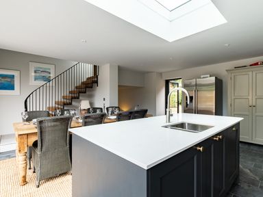 A kitchen and dining area with a central island, sink, dining table with chairs, staircase, refrigerator, and cabinets at Porthilly Greys in Rock