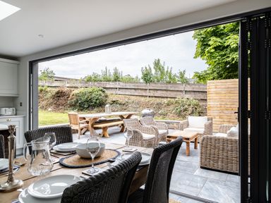 A dining table set with plates and glasses beside an outdoor patio with wicker chairs and wooden tables at Porthilly Greys in Rock