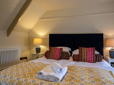 A bedroom with a double bed with patterned cushions and folded towels on a blanket at Porthilly Greys in Rock