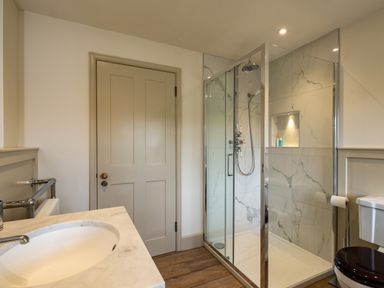 A bathroom with a sink countertop, a wooden door, a glass shower enclosure, and a toilet at Porthilly Greys in Rock