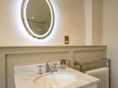 A bathroom sink with marble countertop and round illuminated mirror at Porthilly Greys in Rock