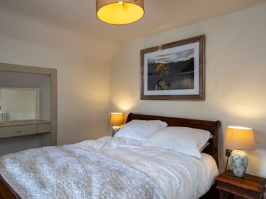 A bedroom with a wooden bed white bedding two bedside tables with lamps and a framed picture on the wall at Porthilly Greys in Rock