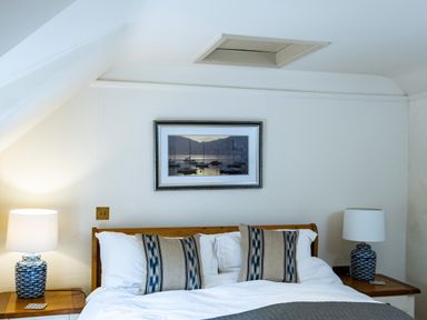 A bedroom with a wooden bed frame two patterned pillows and lamps on bedside tables at Porthilly Greys in Rock