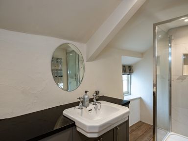 A bathroom with a sink and mirror next to a shower and a small window at Porthilly Greys in Rock