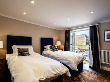 A bedroom with two single beds bedside tables lamps open doors to a garden at Porthilly Greys in Rock