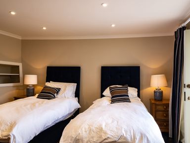 A bedroom with two single beds each with a striped pillow two bedside tables with lamps at Porthilly Greys in Rock