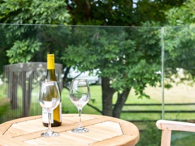 A bottle of white wine and two empty wine glasses on a wooden table outside with trees and greenery in the background at Porthilly Greys in Rock