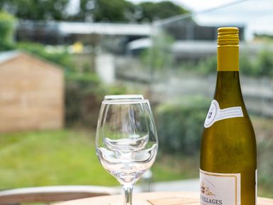 A bottle of white wine and two empty wine glasses on a wooden table outside