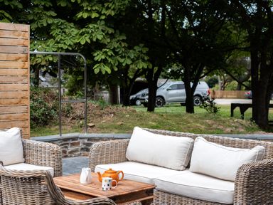 An outdoor seating area with wicker furniture a wooden table an orange teapot and a white mug at Porthilly Greys in Rock