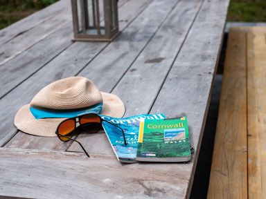 A wooden outdoor table with a hat sunglasses and Cornwall guidebooks at Porthilly Greys in Rock