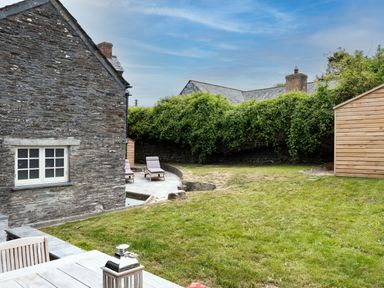 A backyard with a stone house outdoor table wooden shed lawn and lounge chairs at Porthilly Greys in Rock
