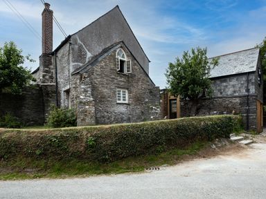 A stone house with a chimney and open windows surrounded by a hedge and trees at Porthilly Greys in Rock