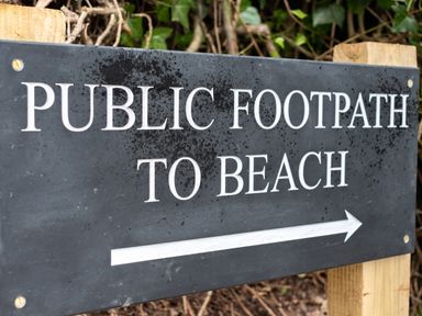 A public footpath to beach sign mounted on wooden posts with vegetation in the background at Porthilly Greys in Rock
