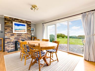 A dining area with a wooden table and chairs near sliding glass doors overlooking a garden at Trebartha Daymer Bay