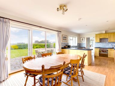 A kitchen and dining area with wooden table and chairs near sliding glass doors opening to a garden at Trebartha in Daymer Bay