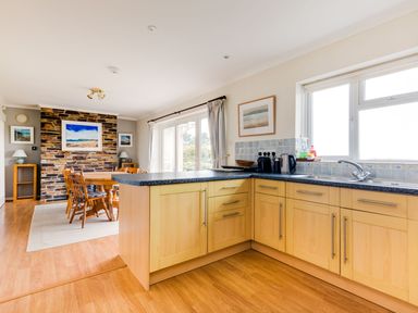 A kitchen with wooden cabinets and a countertop next to a dining area with a wooden table and chairs at Trebartha in Daymer Bay