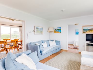 A living room with blue sofas white cushions a striped rug and a floor lamp next to a dining area with wooden chairs at Trebartha in Daymer Bay