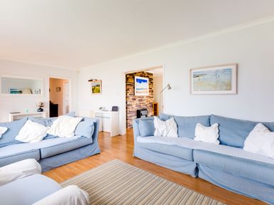 A living room with two blue sofas with white cushions a striped rug and framed pictures on the walls at Trebartha in Daymer Bay
