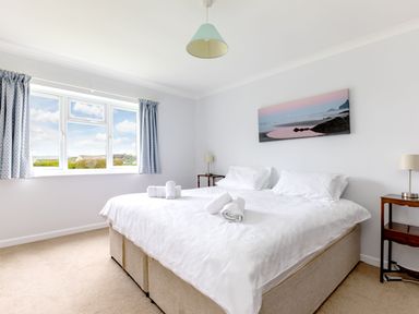 A bedroom with a double bed and rolled towels on top two bedside tables with lamps and a window with curtains at Trebartha in Daymer Bay