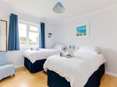 A bedroom with two beds blue curtains and a chair at Trebartha in Daymer Bay