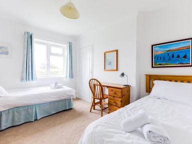 A bedroom with two beds a wooden desk and chair a window with blue curtains and a painting above a bed at Trebartha in Daymer Bay