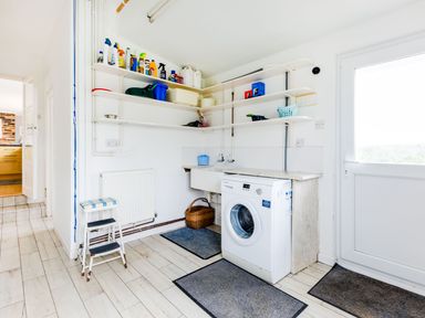 A laundry room with washing machine shelves holding cleaning supplies and a stool at Trebartha in Daymer Bay