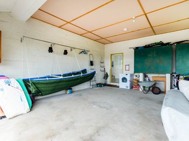 A storage room with a washing machine sailboards a wheelbarrow and green cabinets at Trebartha in Daymer Bay
