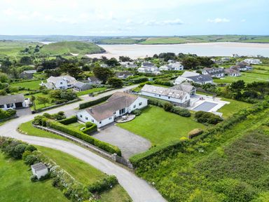 An aerial view of houses with lawns trees and hedges near a body of water at Trebartha in Daymer Bay