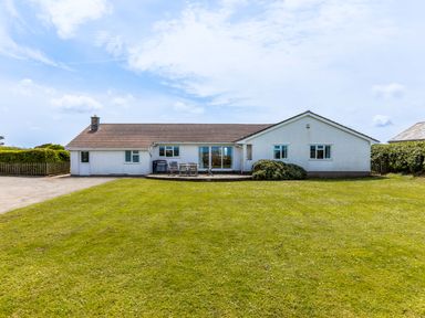 A detached house with a patio table and chairs on a lawn at Trebartha in Daymer Bay