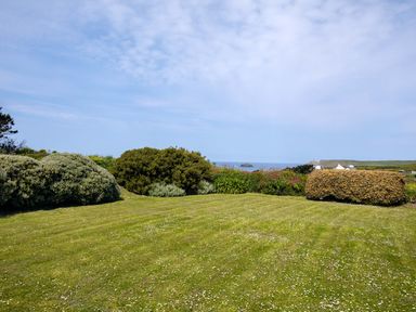 A grassy garden with shrubs and a view of the sea at Trebartha in Daymer Bay