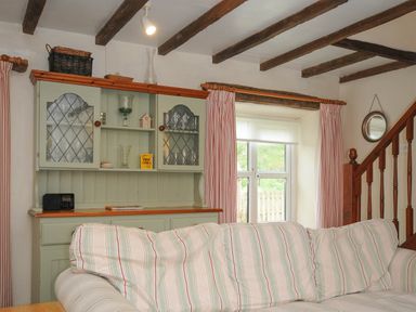 A sitting room with a striped sofa a wooden cabinet with glass doors and stair railing at The Granary Rock