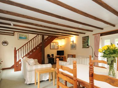 A living room with striped sofas a dining table with yellow flowers wooden beams on ceiling and a staircase at The Granary Rock