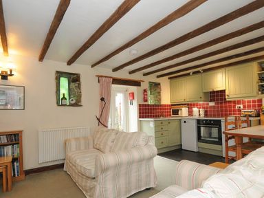 An open plan living room and kitchen with striped sofas wooden beams and green kitchen cabinets at The Granary in Rock