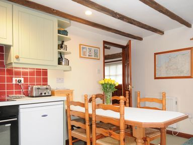 A kitchen with a dining table and chairs a vase with yellow flowers and red tiled backsplash at The Granary in Rock
